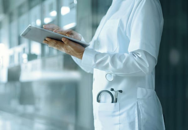A doctor in a white coat using a tablet, with a stethoscope visible in the pocket.