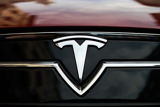 Close-up of a Tesla logo on the front of a red and black electric car.